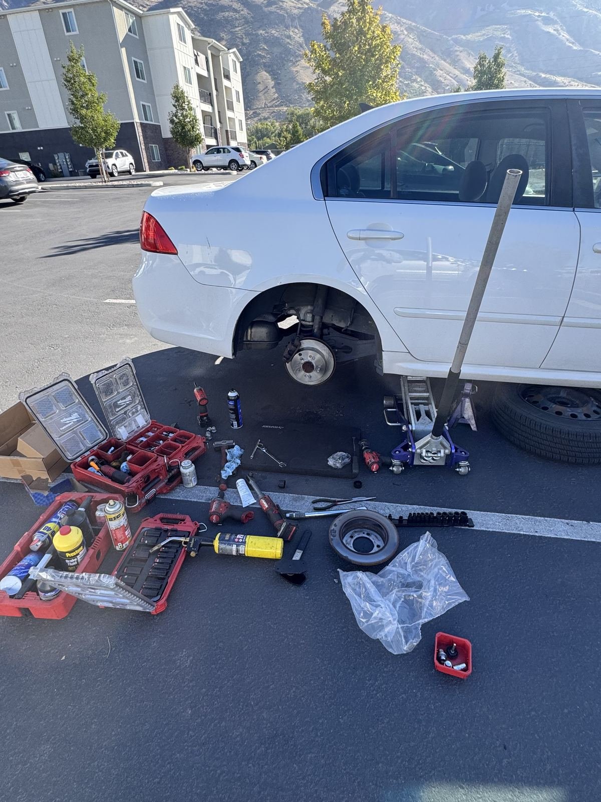 Brake job on a white sedan in an apartment parking lot with mountains behind it